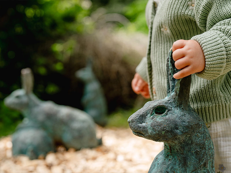 Child exploring tactile hare sculptures in the garden.