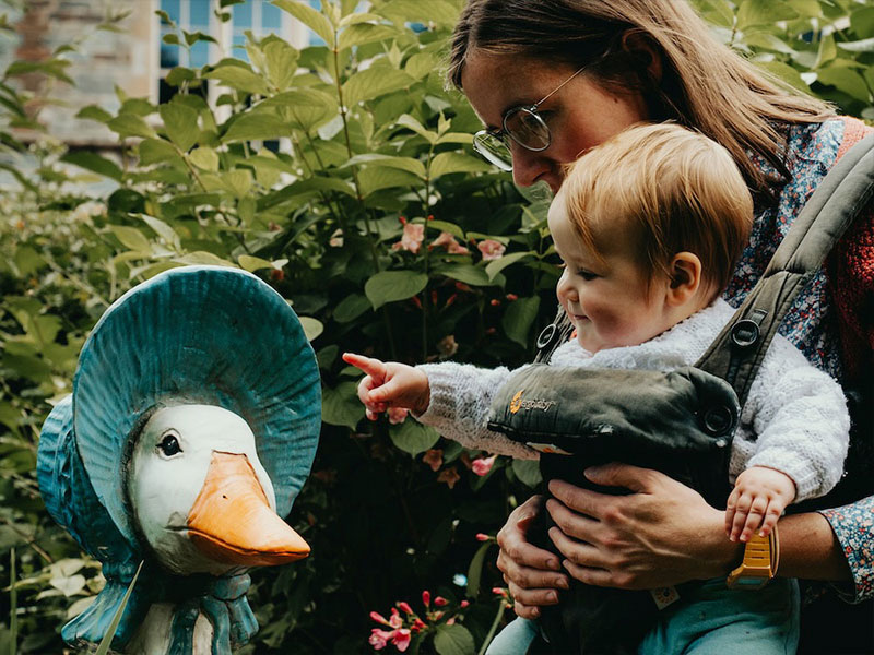 Young child interacting with a Jemima Puddle-Duck sculpture on the Beatrix Potter Garden Trail
