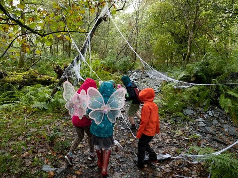 Children in fairy wings exploring a Halloween seasonal trail with giant cobweb decorations at Loch Lomond Faerie Trail