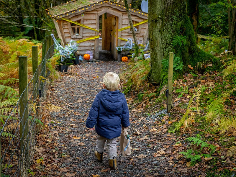 Child approaching a decorated fairy house on a Halloween seasonal trail at Loch Lomond Faerie Trail