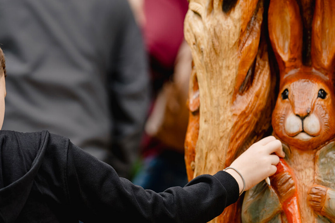 Child touching a tactile rabbit sculpture on the Beatrix Potter Garden Trail